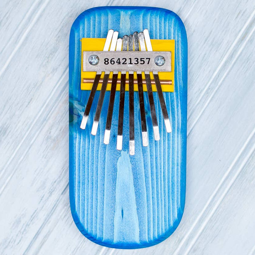 Blue thumb piano with eight metal tines on a light gray textured background
