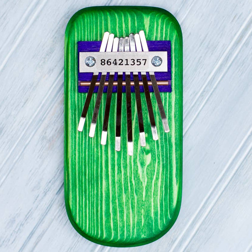 Green wooden thumb piano with eight metal keys on a light gray textured background