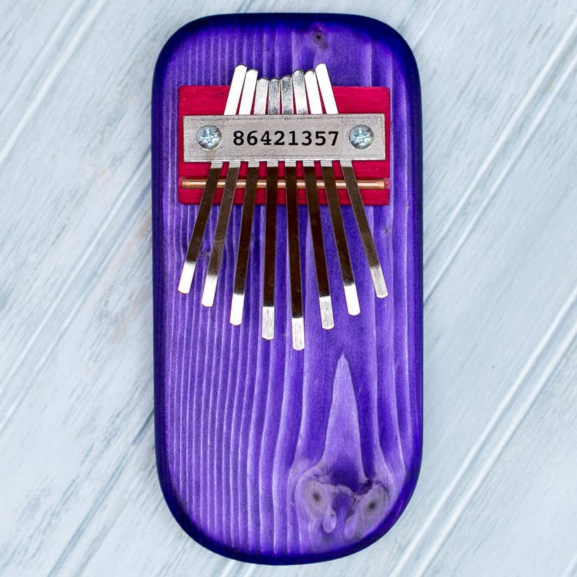 Purple thumb piano with eight metal tines on a light gray textured 