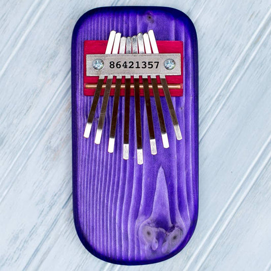 Purple thumb piano with eight metal tines on a light gray textured 